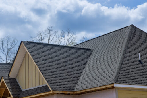 Close-up view of medium gray asphalt shingles on a home with saffron-colored board-and-batten siding and multiple roof peaks