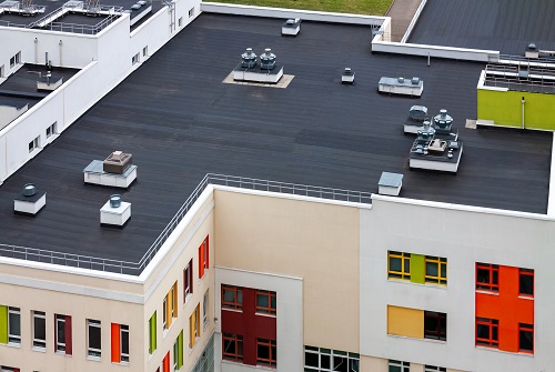 Top view dark flat roof with air conditioners and hydro insulation membranes on a modern apartment building in a residential area.