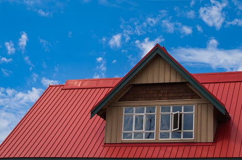 Red roof with dormer in the blue sky background.