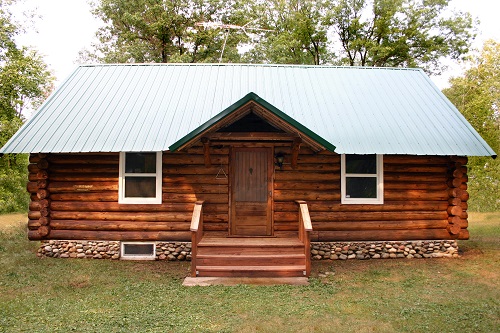 A little rustic log cabin in the woods with a metal roof. 