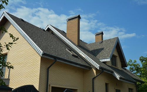 An asphalt shingled roof with skylights, attic windows, chimneys, fascias, and a roof gutter. 